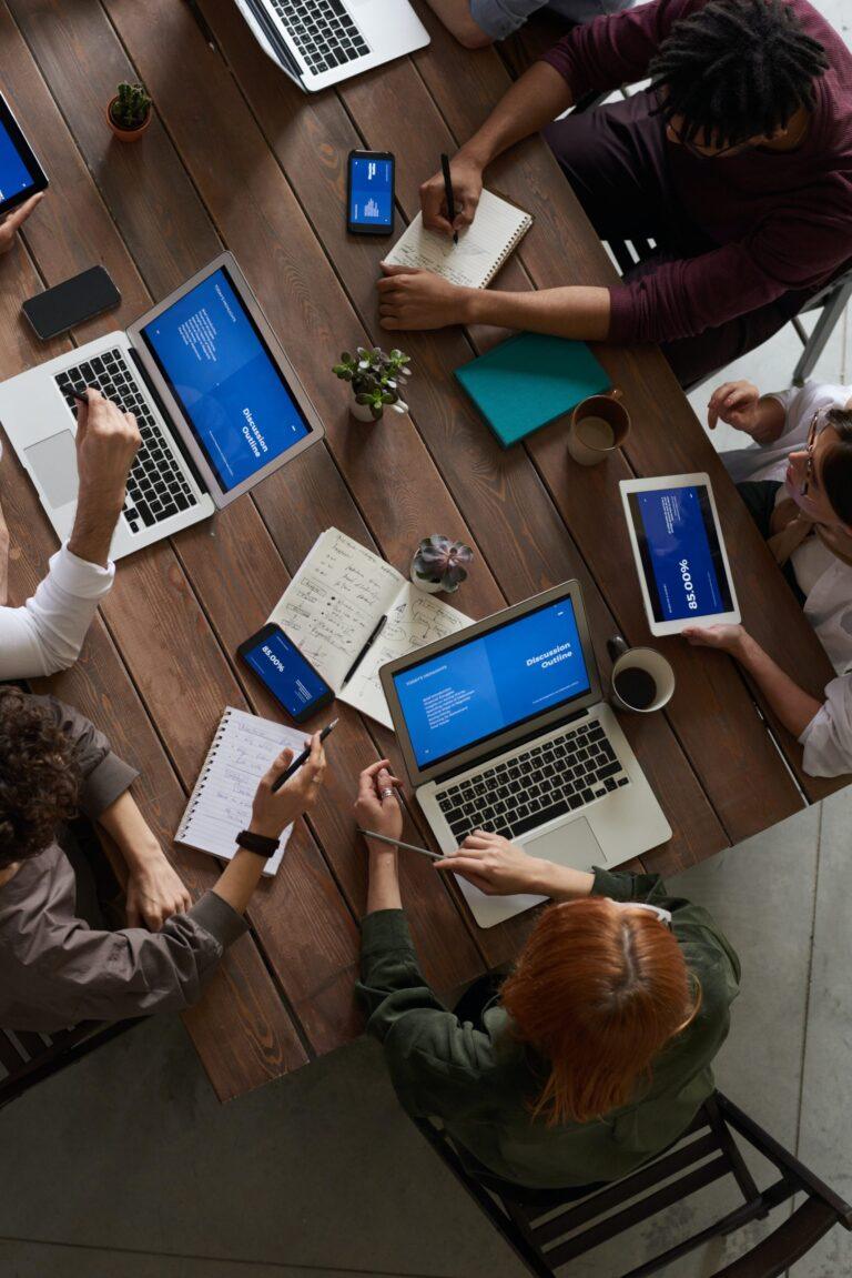 a group of people sitting around a table working on laptops