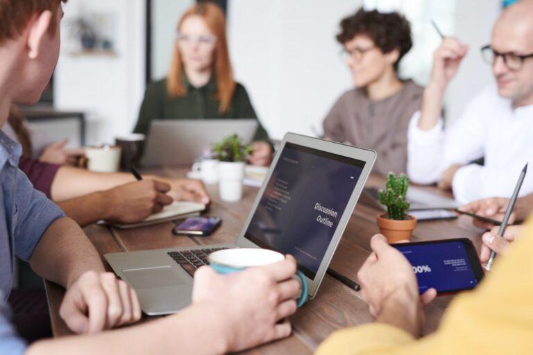 a group of people sitting around a table with laptops