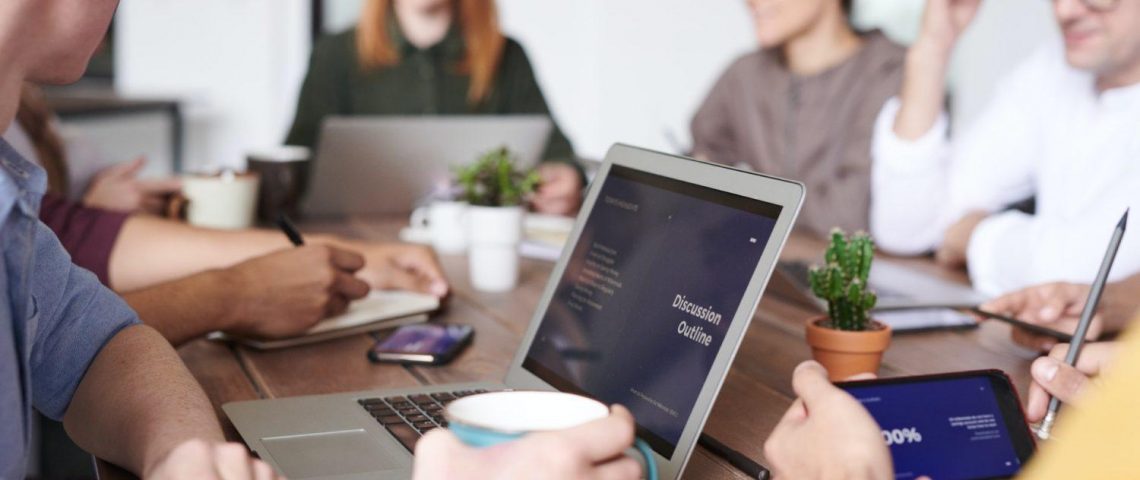 a group of people sitting around a table with laptops