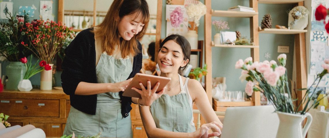 two women sitting at a table looking at a laptop