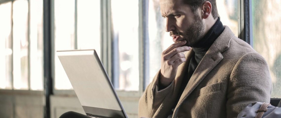 man holding his chin facing laptop computer